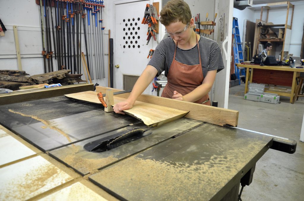 Before Anneloes mitered the longer portion of our slab, she cross cut the slab into two portions: the long one, which later became the coffee table’s top while the shorter one ended up as the leg. To support cross cutting, then mitering the top’s bank we used an oak fence screwed onto two miter gauges. The two gauges provided adequate stability for a safe cross cutting of our thick maple slab.